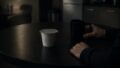 A sealed yogurt sits on a dark break room table while a seated person holds the mug