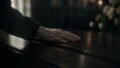 A hand rests on a polished wooden coffin in soft natural light
