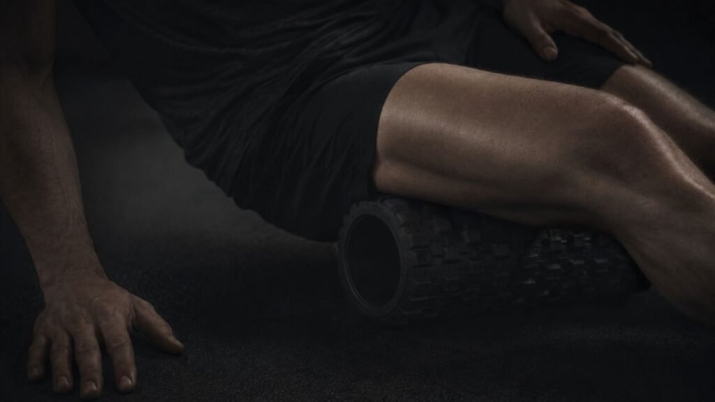 A person uses a black foam roller beneath one thigh, with one hand on the floor