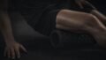 A person uses a black foam roller beneath one thigh, with one hand on the floor