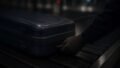 A gloved hand grips the handle of a blue hard-shell suitcase as it moves along an airport baggage conveyor belt