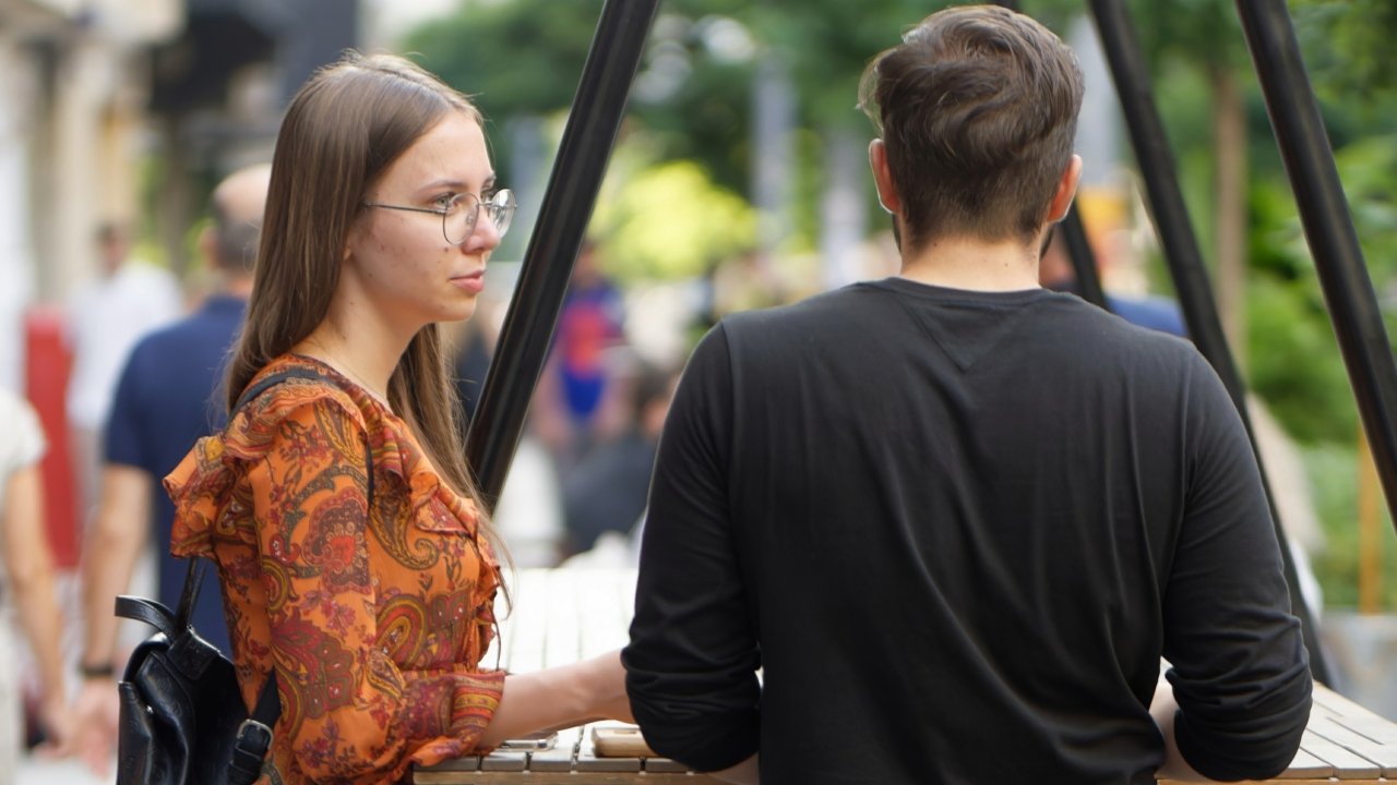 Two people facing each other across an outdoor table during a conversation