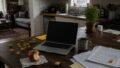 Laptop, work papers, building bricks, a bitten apple and a mug sharing a wooden kitchen table in late-afternoon light
