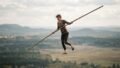 A tightrope walker balancing with a long pole while crossing a suspended rope