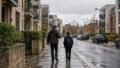 A father and his young son walk along a wet pavement past modern apartment buildings in Edinburgh